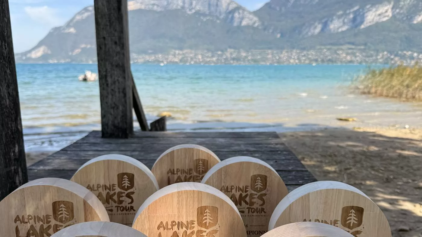 Les huit trophées en bois gravés du classement général Alpine Lakes Tour 2026, posés sur un ponton au bord du lac